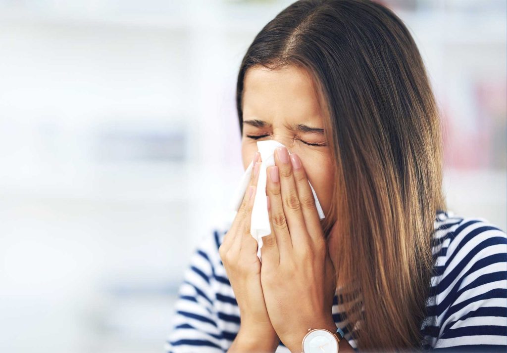 Woman sneezing into a tissue, a common sign of poor indoor air quality in Modesto homes.