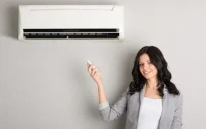 Woman using remote control to operate a ductless mini-split HVAC system on a wall, illustrating efficient climate control for home additions and conversions in Manteca, CA.