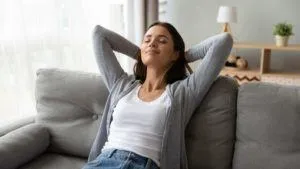 Woman relaxing on a couch with arms behind her head, enjoying a comfortable indoor environment, emphasizing the importance of good indoor air quality in homes.