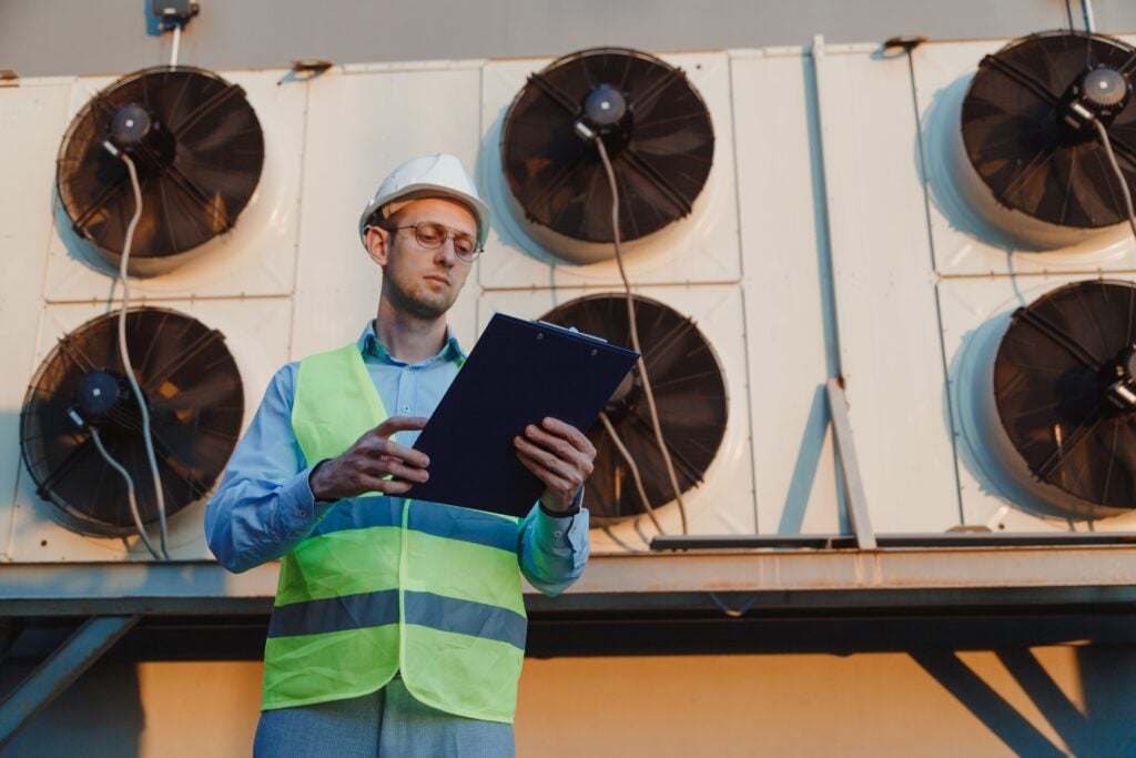 HVAC engineer with a clipboard checking commercial condensing units while pricing a new construction HVAC job