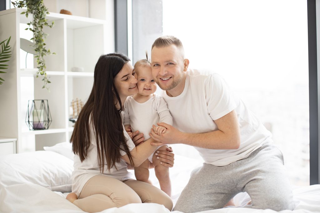 Cheerful parents embracing their young daughter in a bright bedroom, symbolizing family comfort and care.