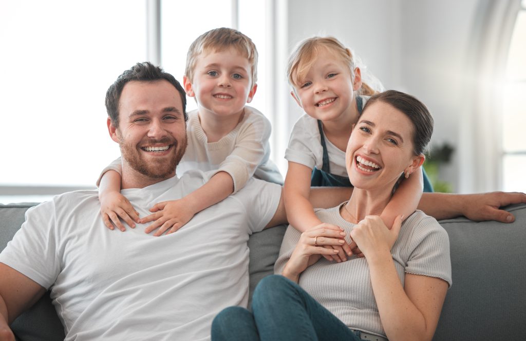 Smiling family of four sitting on a couch, showcasing a happy atmosphere, representing comfort and home life, relevant to Dycus Heating & Air's focus on providing reliable HVAC services for family comfort in Manteca.