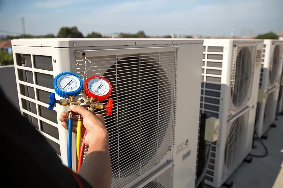 Technician holding HVAC gauge set in front of commercial air conditioning units, illustrating Dycus Heating and Air Conditioning's expertise in HVAC services.