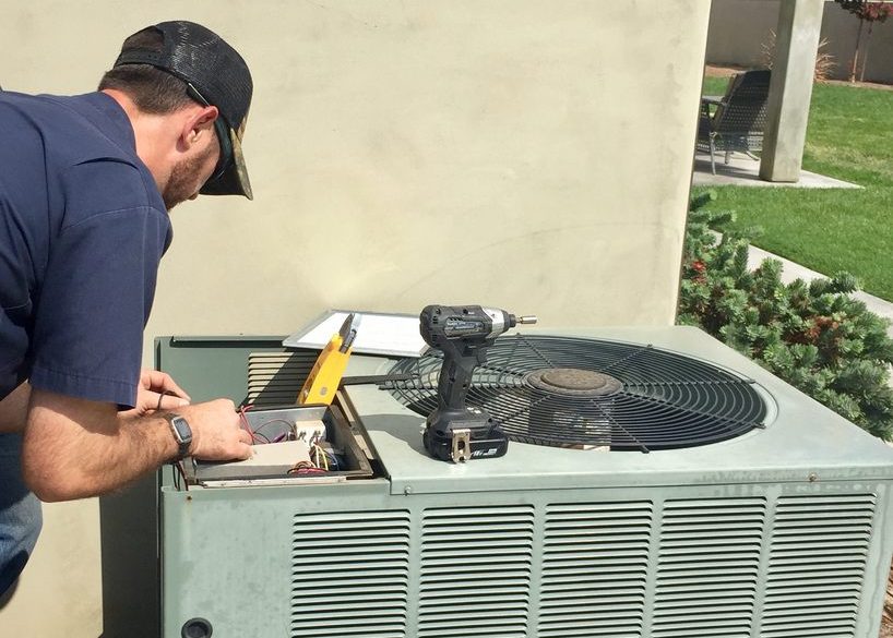HVAC technician repairing air conditioning unit, tools including drill and multimeter, residential setting in Modesto, CA.