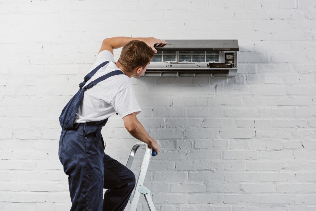 Repair technician adjusting ductless mini split air conditioning unit on wall, showcasing expertise in HVAC services for efficient home climate control.