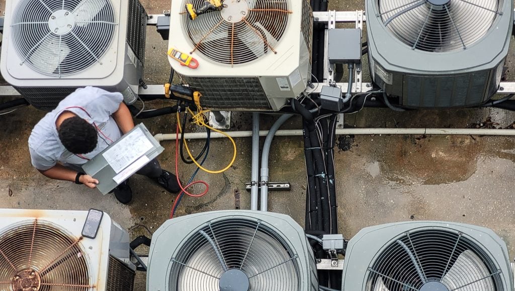 HVAC technician writing up a commercial replacement quote on a clipboard beside rooftop units in Modesto, CA