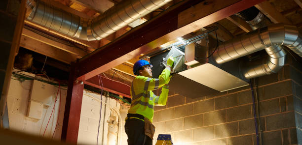 HVAC technician in safety gear installing air ducts in a new construction site, emphasizing professional HVAC services for new builds in Modesto, CA.