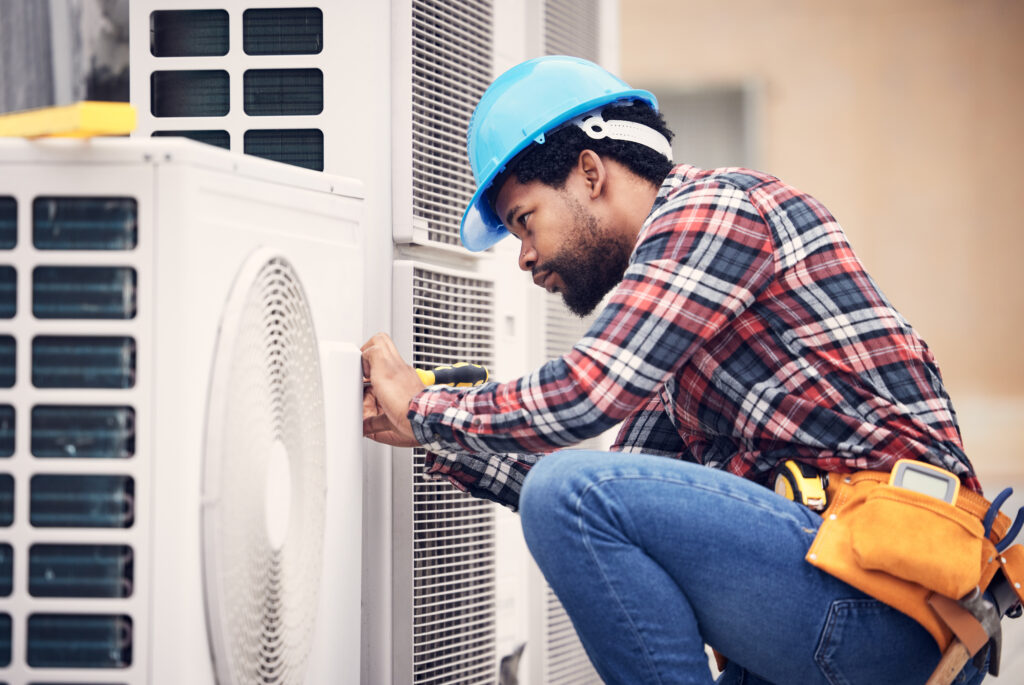 HVAC technician repairing commercial air conditioning unit, wearing blue hard hat and plaid shirt, focused on maintenance tasks in Modesto, CA.